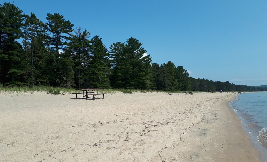 a large white sand beach stretches along the water with green trees behind the beach