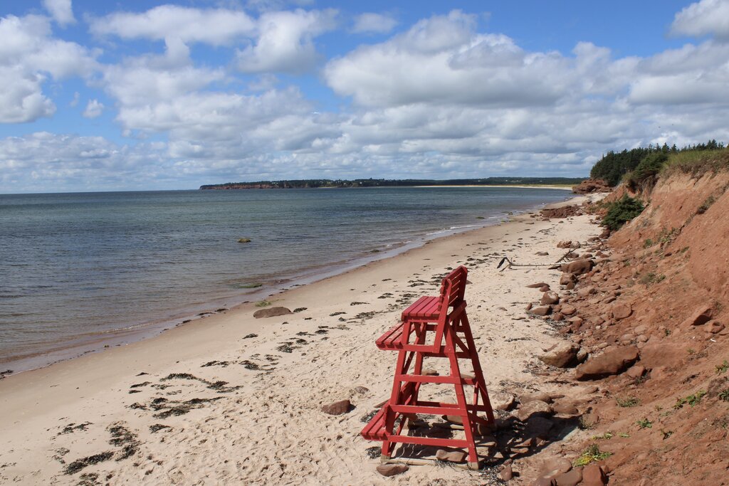 red lifeguard chair on white sand beach with red cliffs in PEI