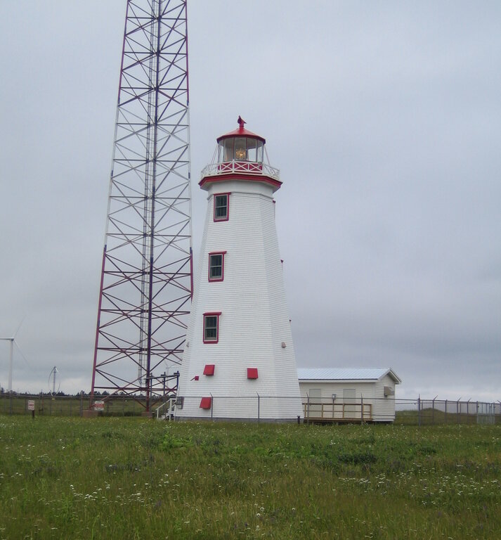 white lighthouse with three windows beside a communications tower
