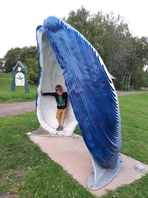 large statue of a blue mussel with a boy standing inside the mussel. 