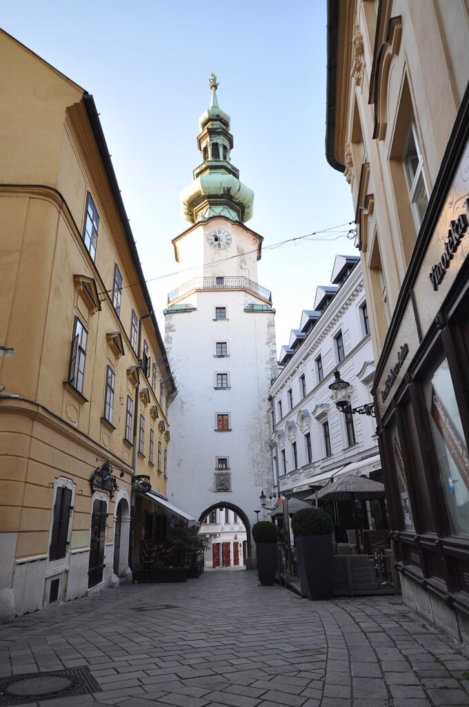 a large white tower with a green top and spire, arched opening at the street level is Michael’s gate