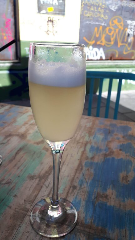 pisco sour served in a champagne glass on a wood table graffiti can be seen on the walls behind