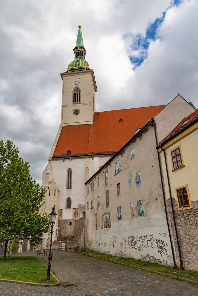 large rectangular church with red roof and green spire which has a replica of the coronation crown on top- there is a small clock underneath the spire. - this is st. martin’s cathedral in bratislava
