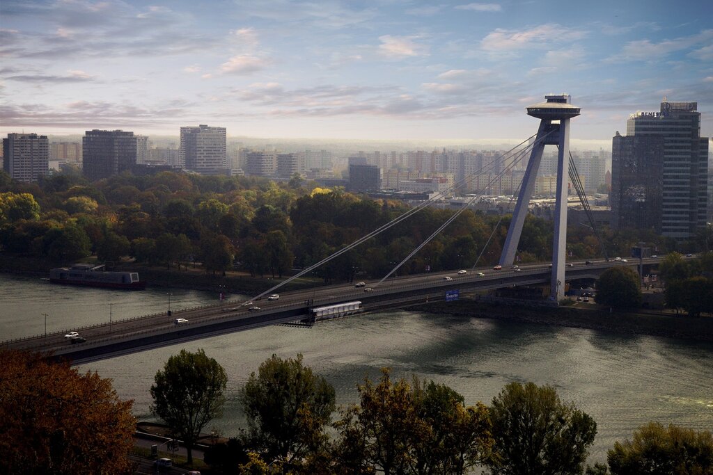 this long suspension bridge crosses the Danube River in Bratislava and only has one pylon, which looks like ufo on top, earning the nickname UFO bridge. apartment buildings and tall office buildings can be seen in the distance on the other side of the river