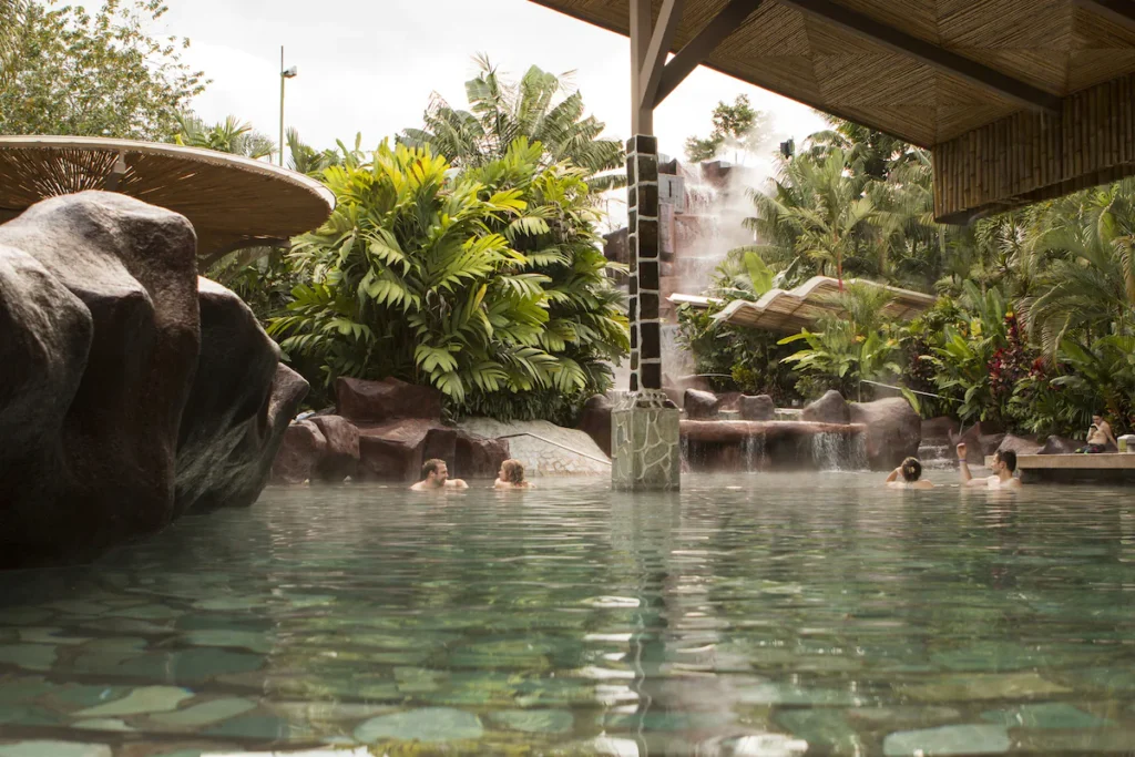 people swimming in a hot spring pool with waterfall and rocks in the background