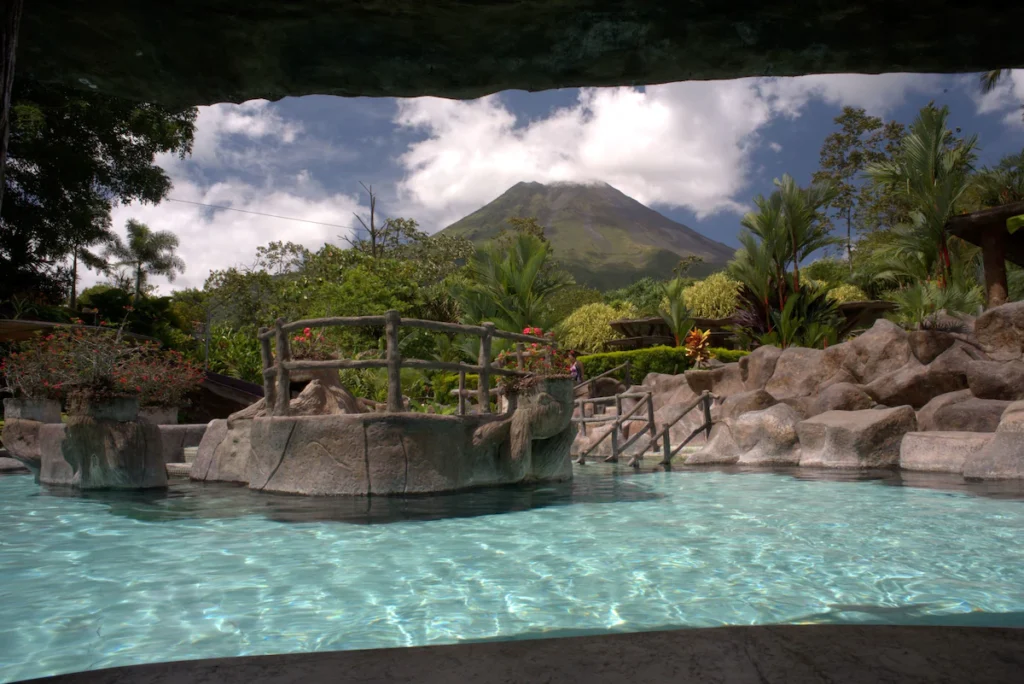 hot spring pool with ladder entering the pool, rock walls surrounding the pool and the volcano in the background