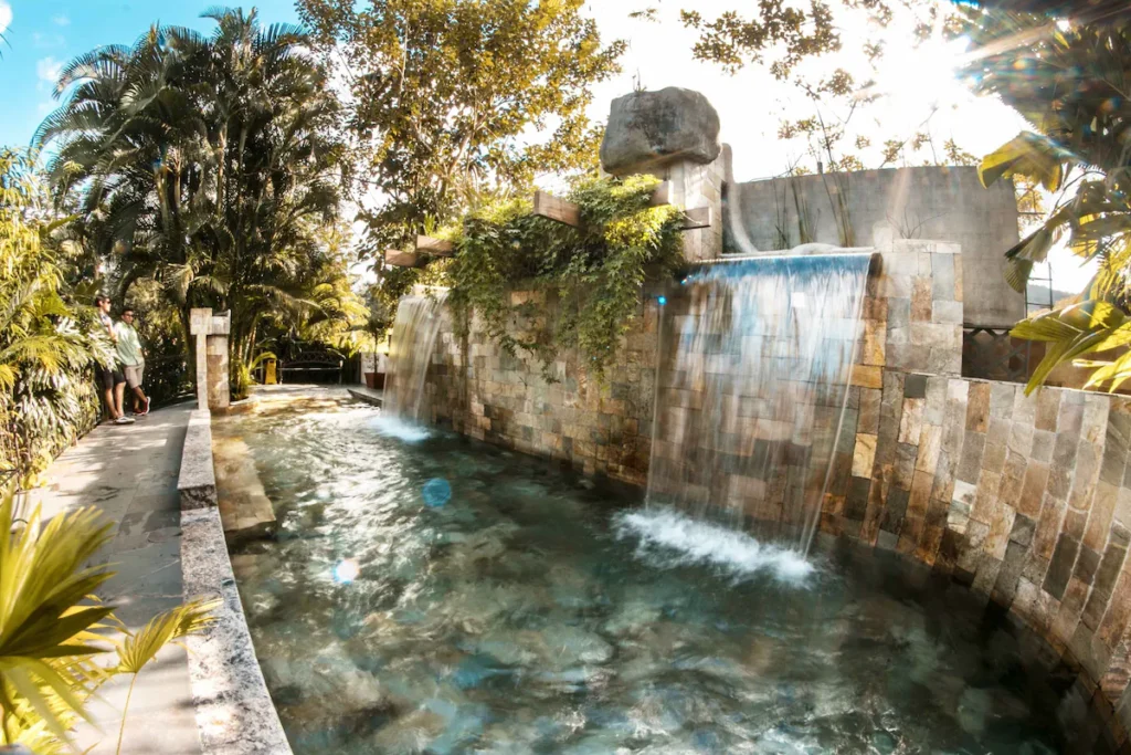 water flowing over a rock wall into a hot spring pool at paradise hot spring in la fortuna Costa Rica