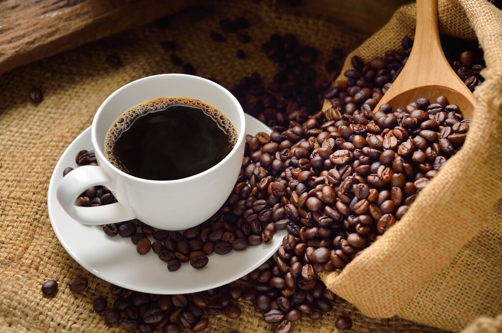 coffee beans spilling out of a bag beside a white cup of coffee