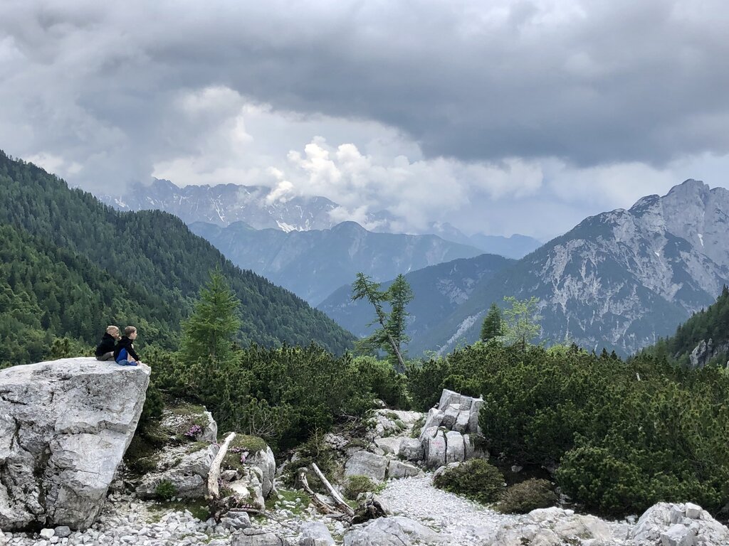 two boys sitting on a rock looking out over the mountains at the highest point while driving the vrsic pass