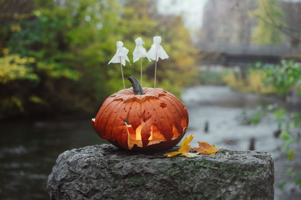 carved pumpkin with three ghost picks on top on a riverbank in Vilnius Lithuania