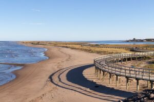 a long boardwalk curves away from the water overtop of a large sand beach in new brunswick