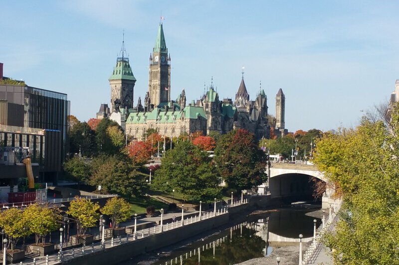 view of ottawa with the green roofs of chateau laurier rising above the trees and the historic rideau canal in the foreground of the photo