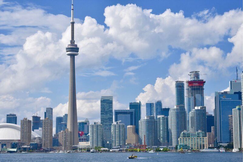 Toronto skyline with the CN Tower rising above modern high-rises, seen from across Lake Ontario on a bright, partly cloudy day. This iconic view highlights one of the top places to visit in Ontario.